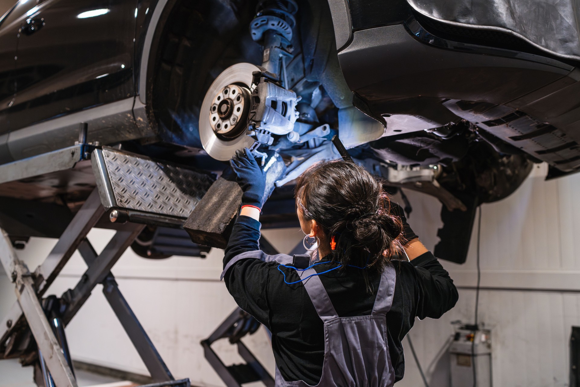 Female mechanic inspecting car brakes on hydraulic lift in repair shop