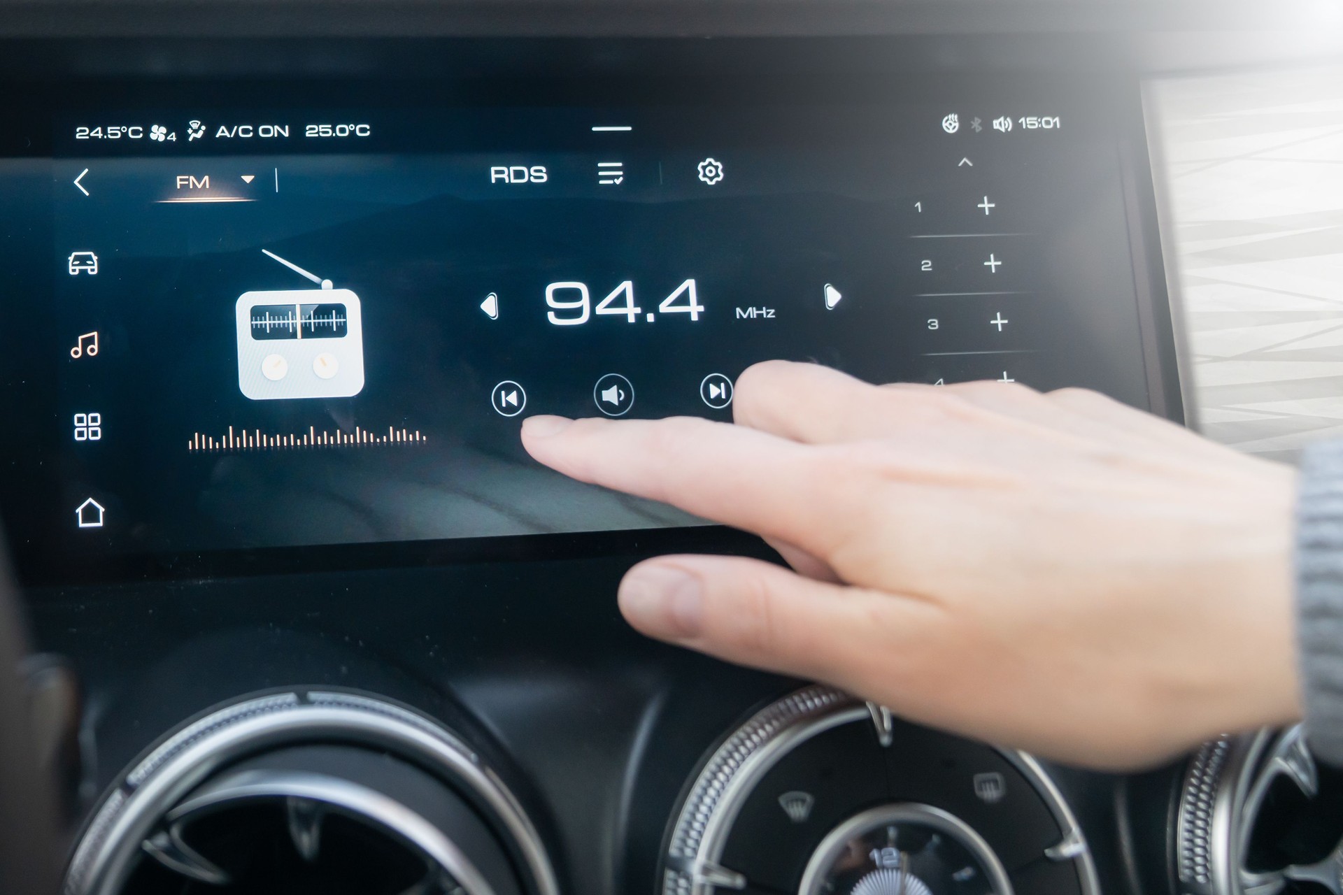 The passenger controls the radio on the car's touchscreen with his finger. An individual adjusts the radio on a sleek car dashboard touchscreen, highlighting convenience and technology.